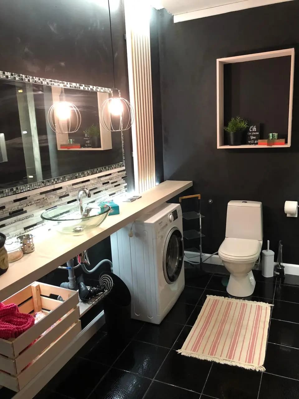 Wide view of the black bath with mosaic backsplash, caged sconces, and the washer tucked under the counter