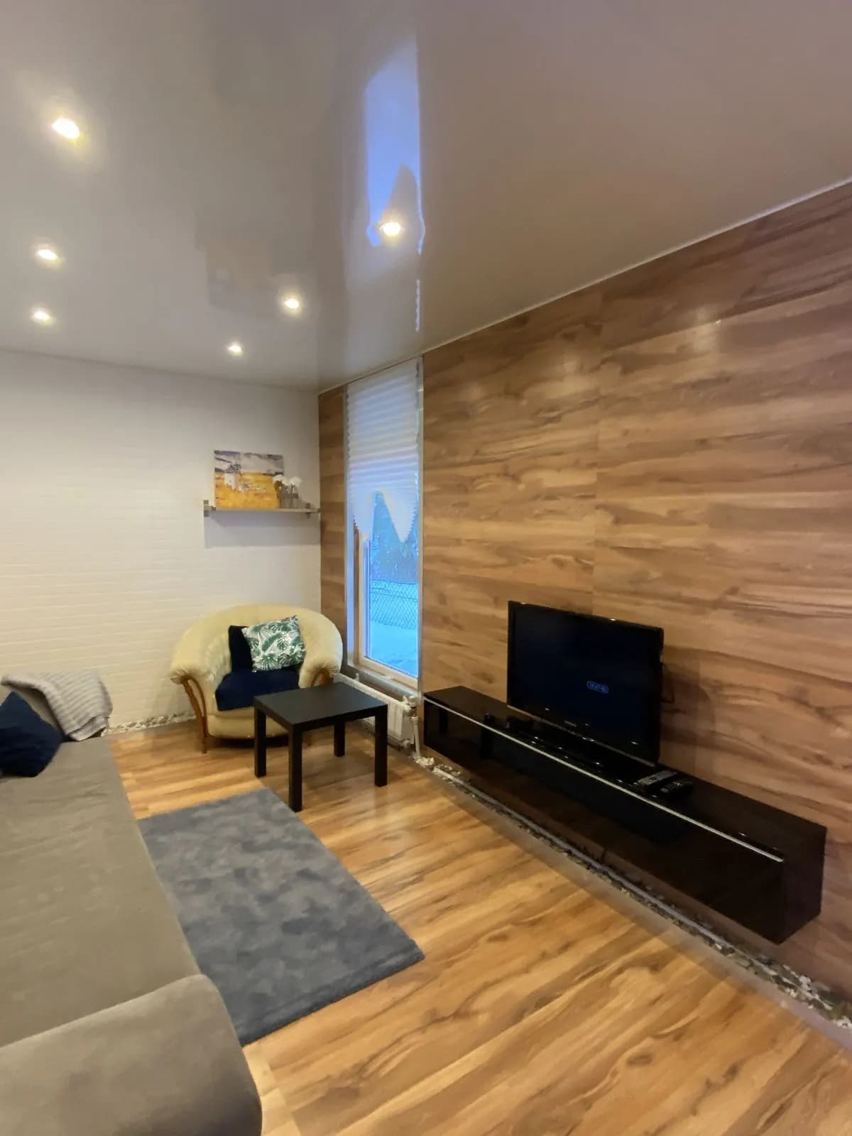 Living room with a grey sofa, charcoal rug, and a low black media unit against a walnut wall
