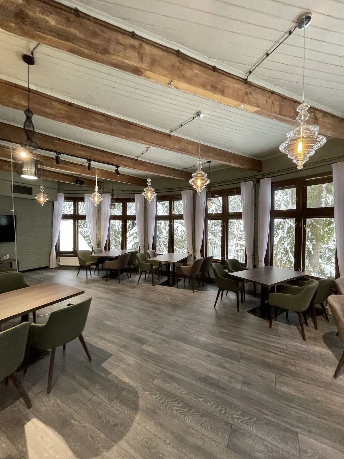 Timber-frame dining room with glass pendant lights, sage walls, and olive upholstered chairs